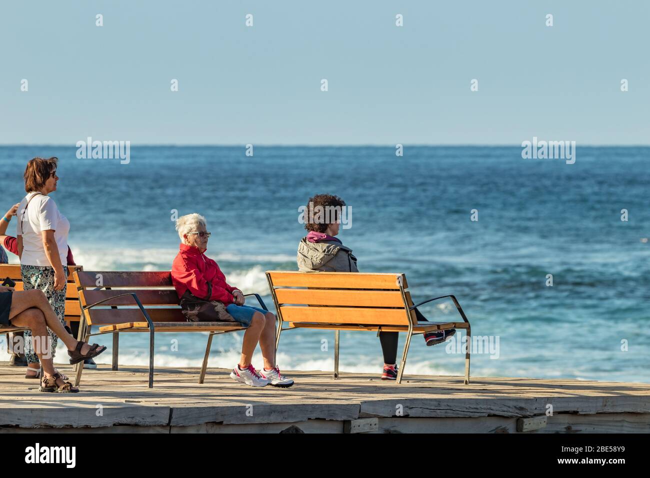 Las Americas,Tenerife, Spain - January 21, 2020: People on the waterfront, walking on promenade and relax sitting on benches near the sea on blue sky Stock Photo