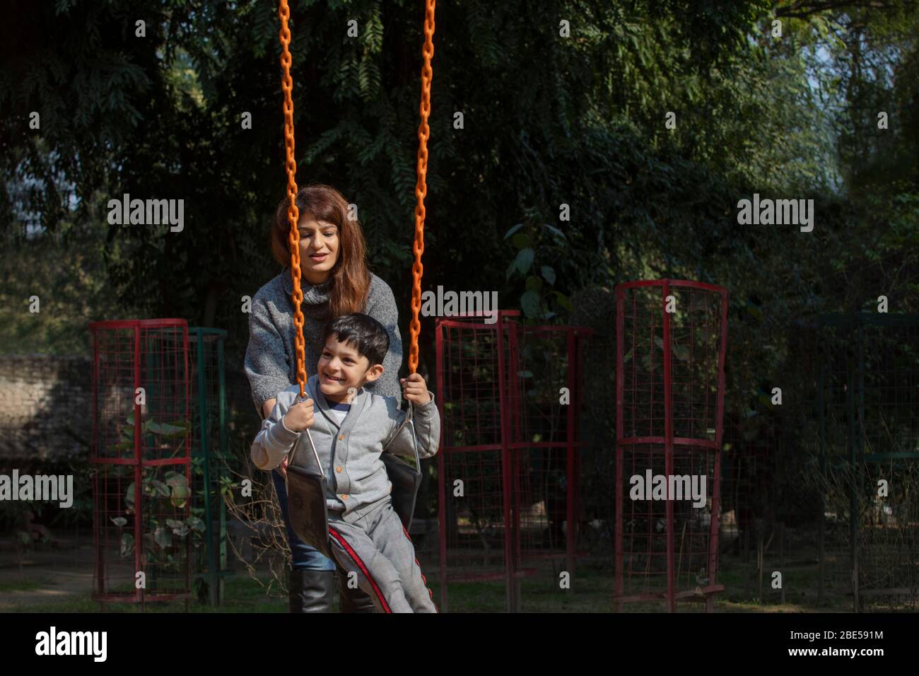 Mother pushing his son on the swings. Stock Photo