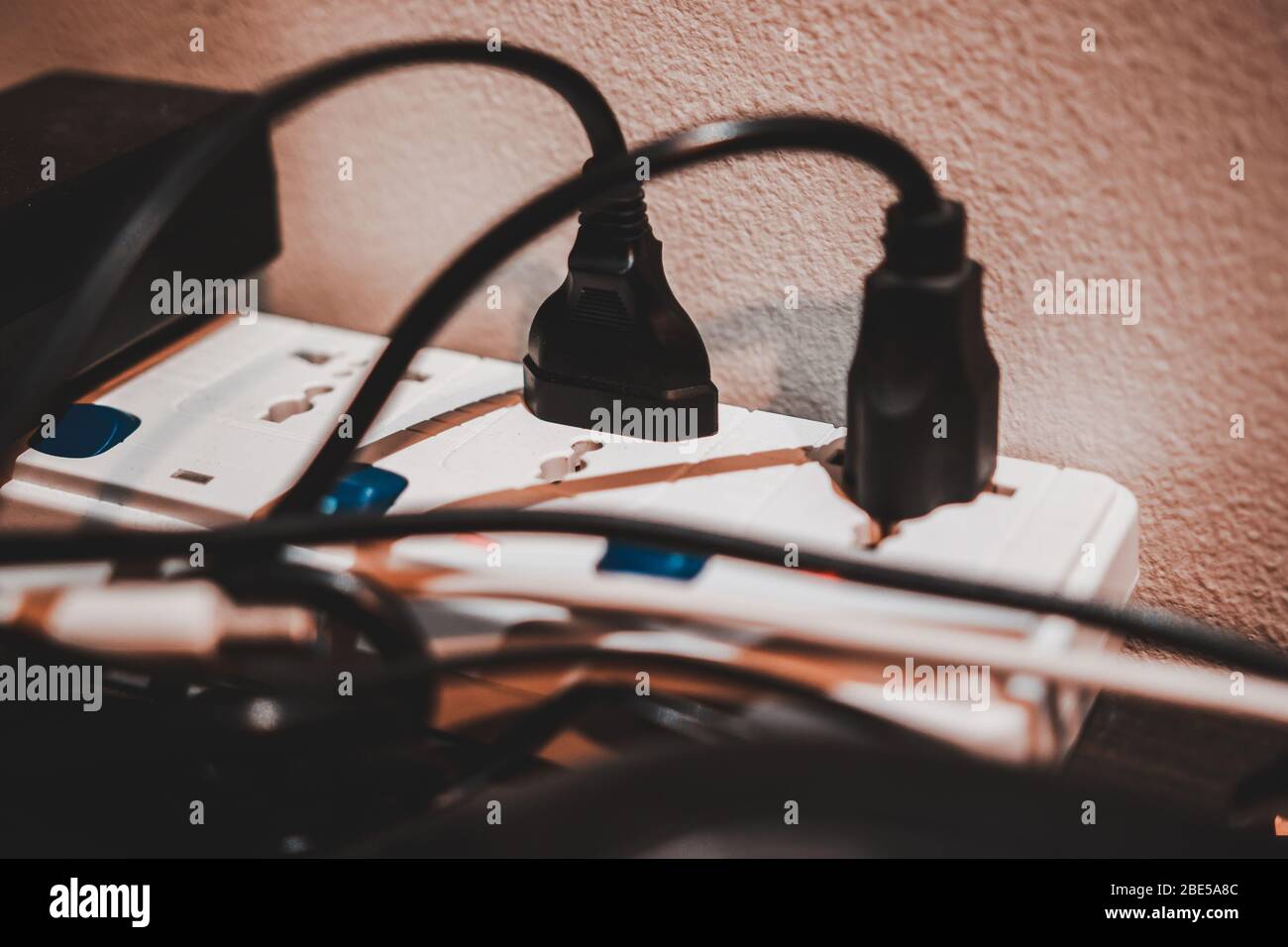 White extension cord on the desk with a lot of electric plugs plugged into  its socket. Might become fire hazard if overloaded Stock Photo - Alamy