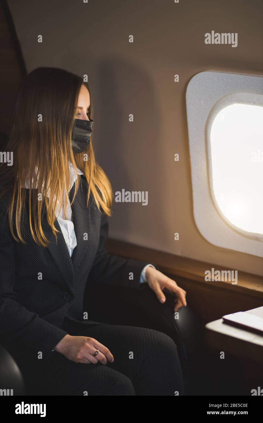Young beautiful business woman sitting on a plane in a black medical mask during a coronavirus pandemic Stock Photo