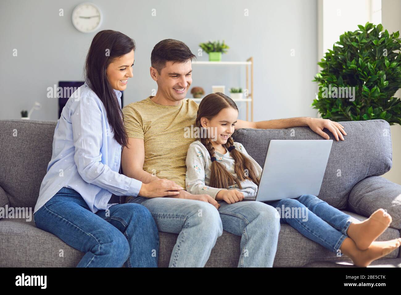 Happy family chatting online using laptop while sitting with baby on sofa at home. Stock Photo