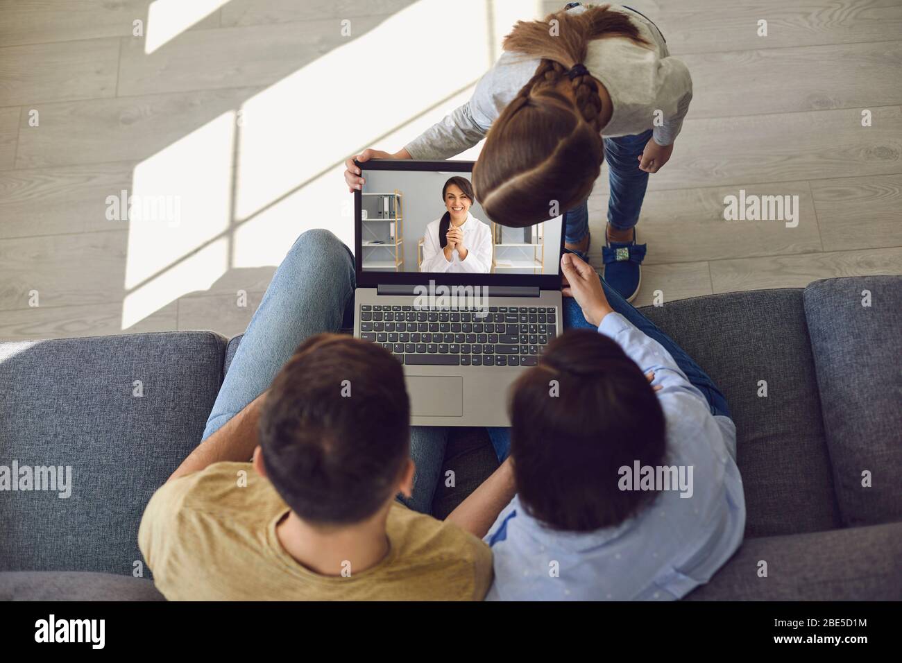 Doctor online. Happy family talks consults with a doctor using a laptop while sitting at home on the couch. Stock Photo
