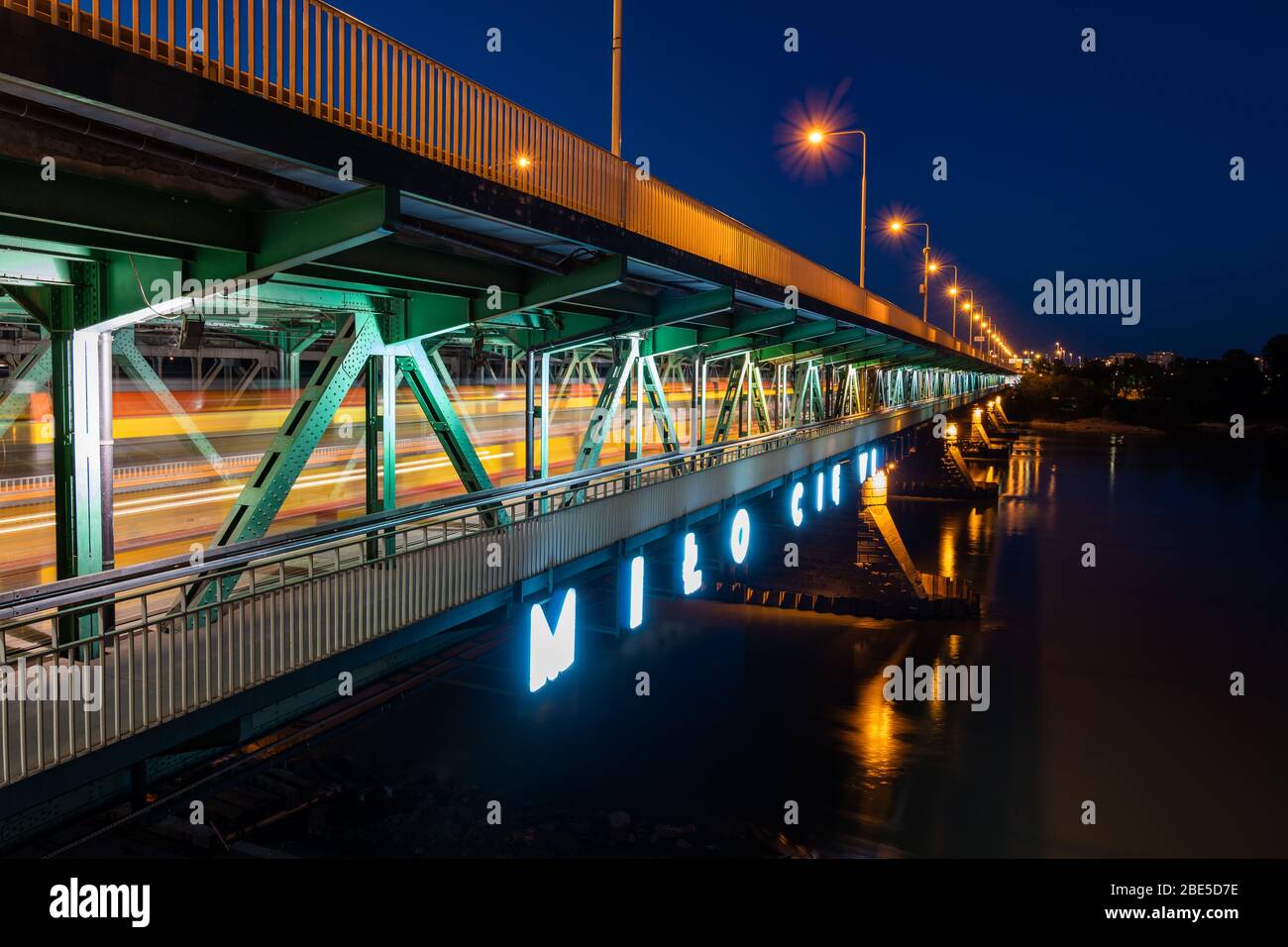 Gdanski Bridge over Vistula river at night in city of Warsaw in Poland, neon sign in Polish - 'Nice To See You', tram light trails on lower level of d Stock Photo