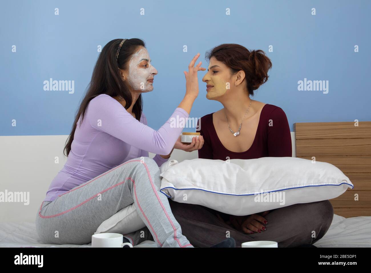 Young woman applying face pack on her sister’s face. Stock Photo