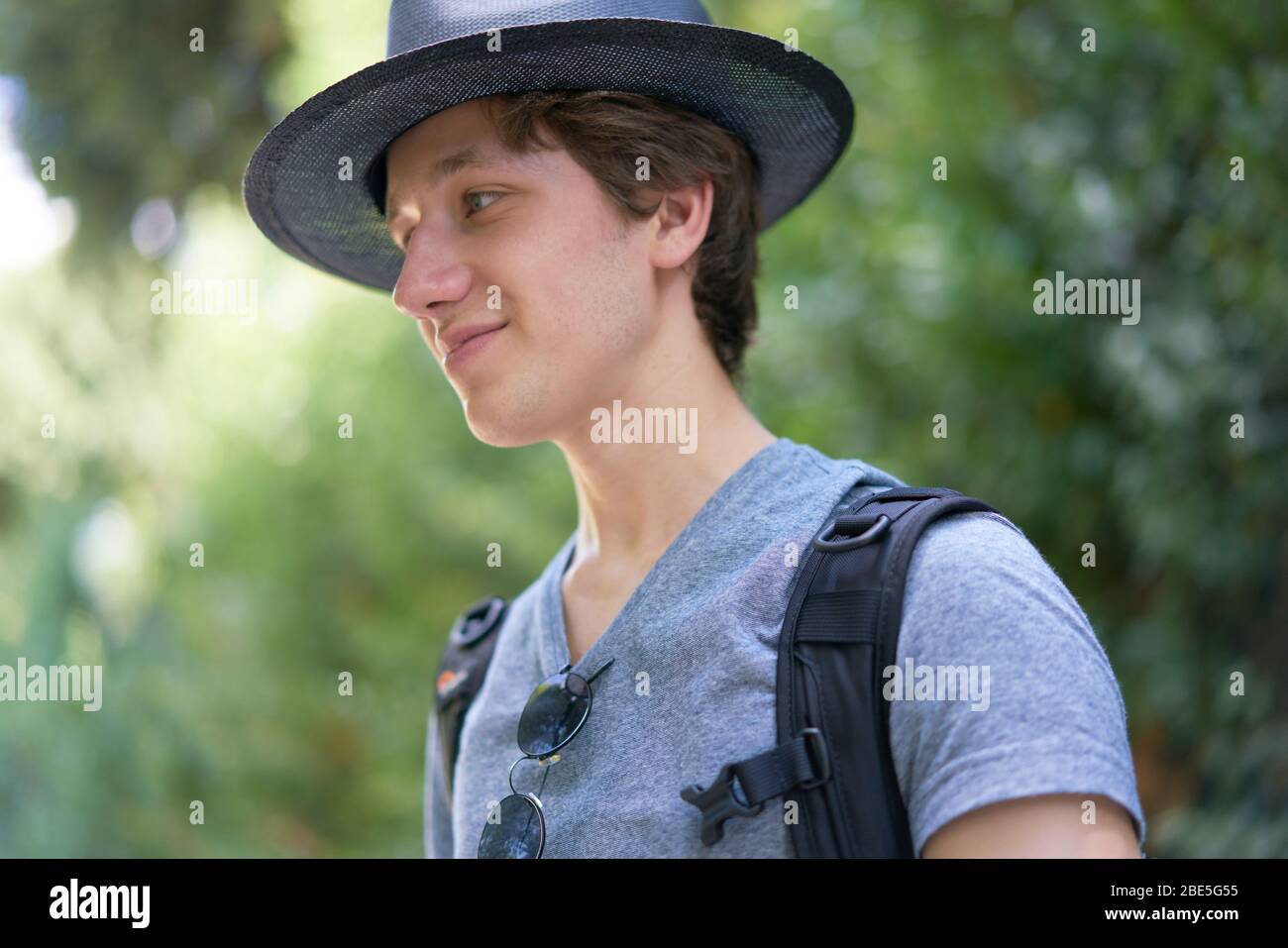 Young handsome man with a hat happily smiling in his summer holidays outside in beautiful greenery Stock Photo