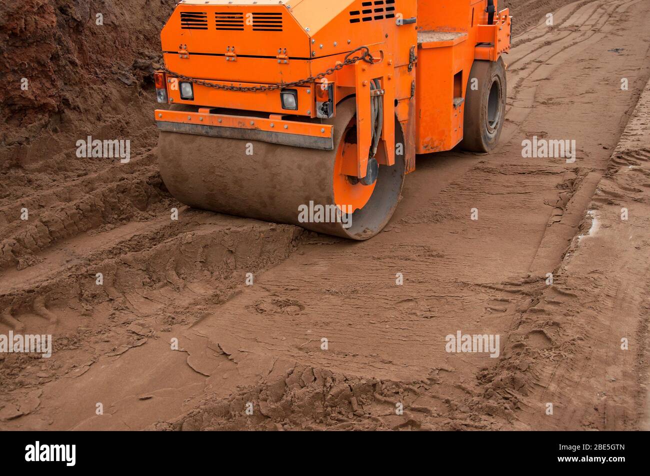 A small road roller rolls soil for a new road. Construction machinery at work. Road construction equipment Stock Photo