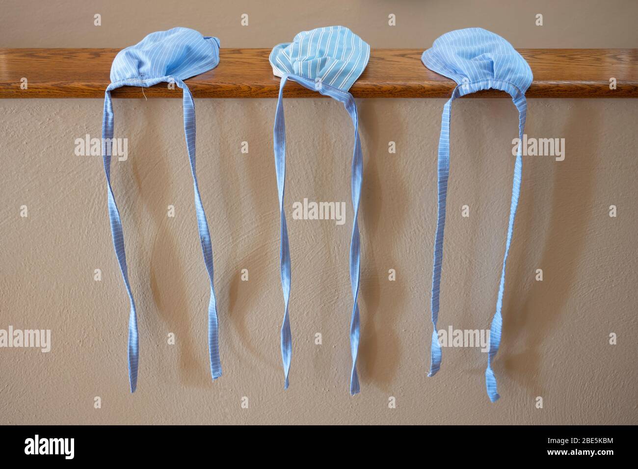 A close-up of three, hand-sewn face masks that were made from blue striped cotton cloth, without elastic-bands, to help prevent the spread of the COVI Stock Photo