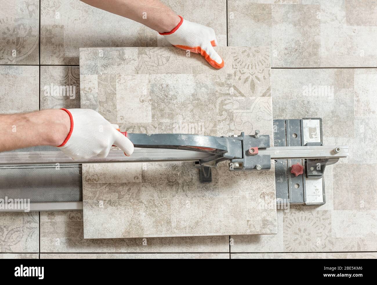 A man is cutting a ceramic tile with a tile cutter. Stock Photo