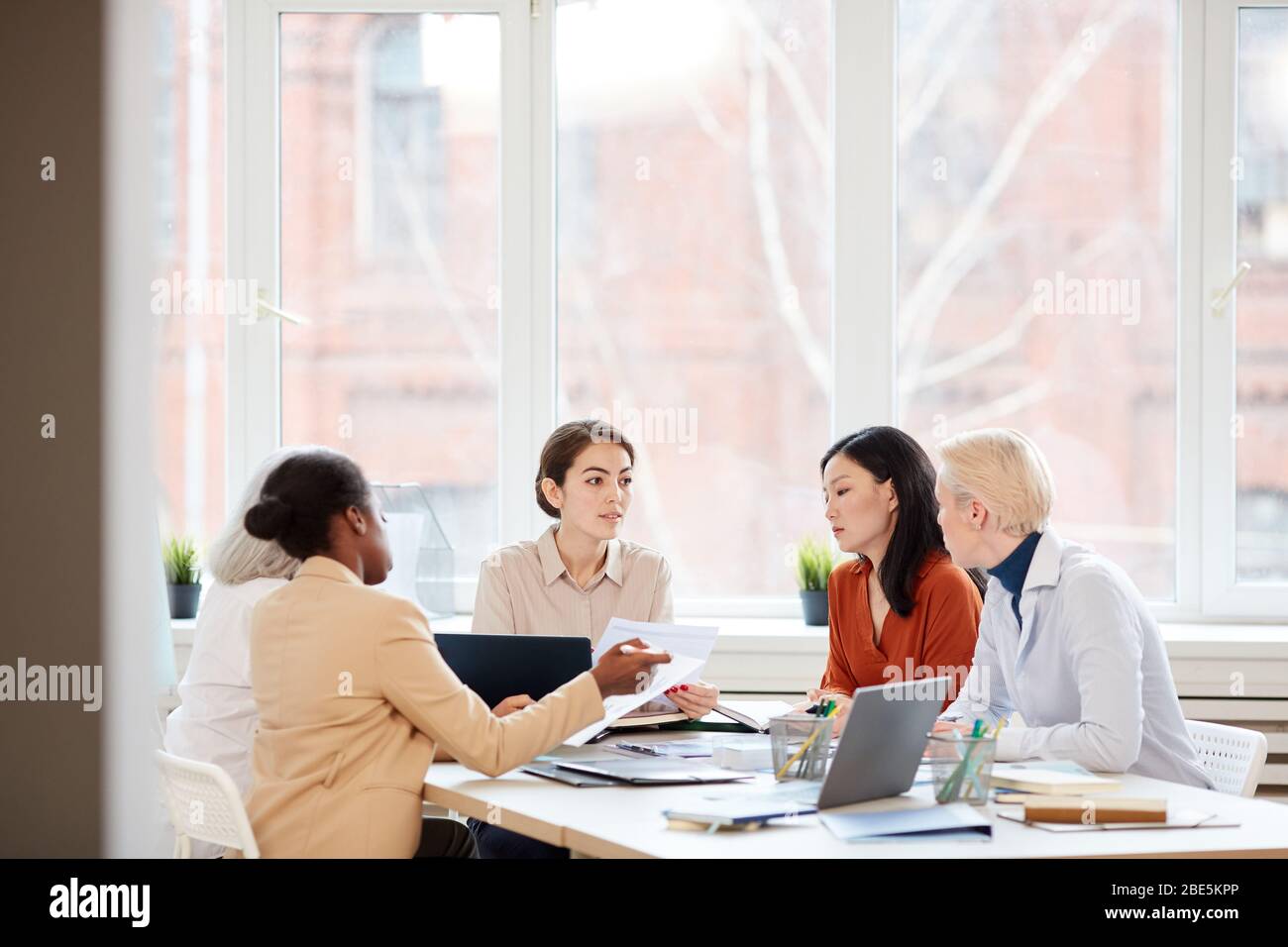 Wide angle view at diverse female business team discussing project while sitting at table during meeting in conference room, copy space Stock Photo