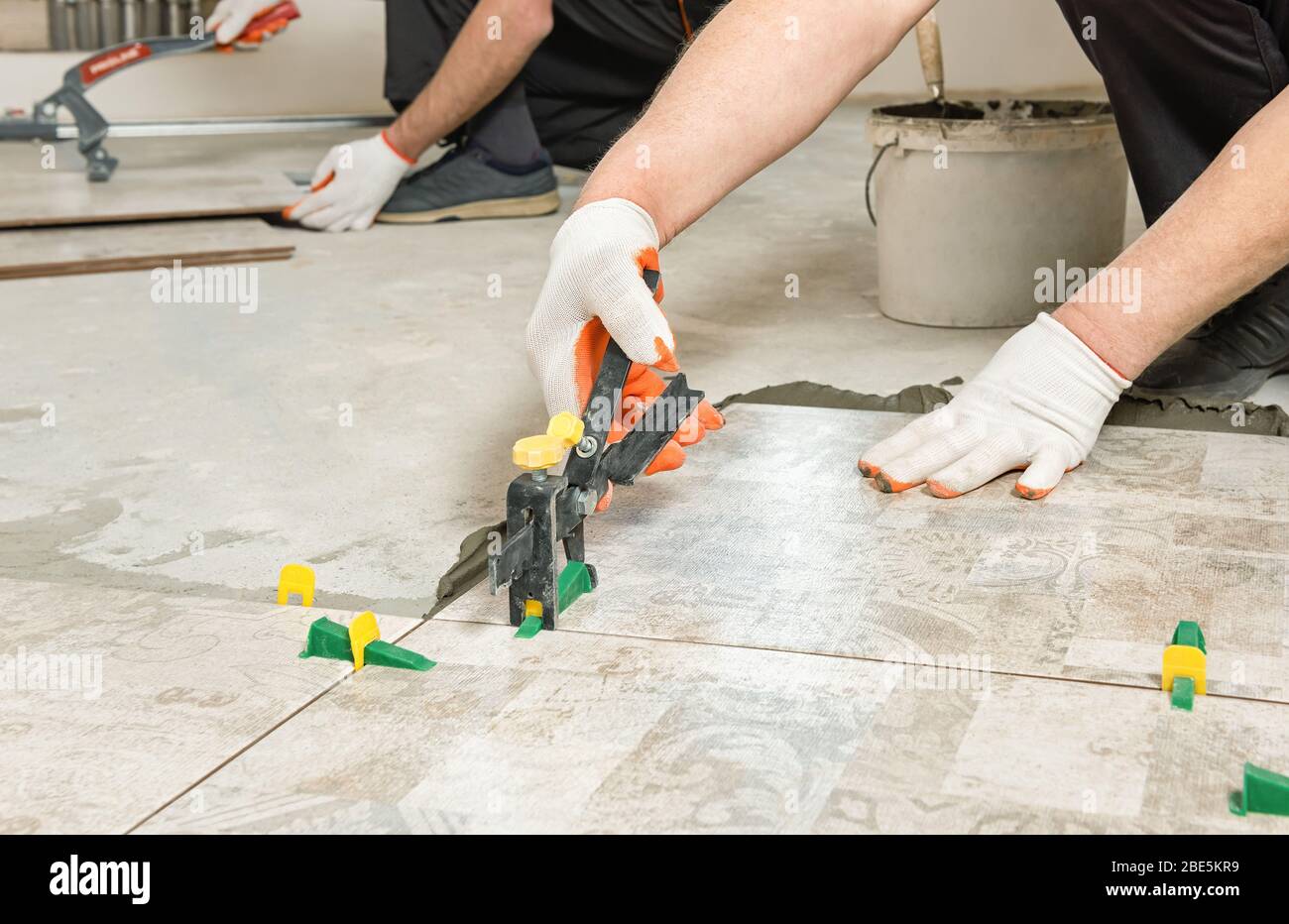 A worker is leveling the ceramic tile with wedges and clips. Stock Photo