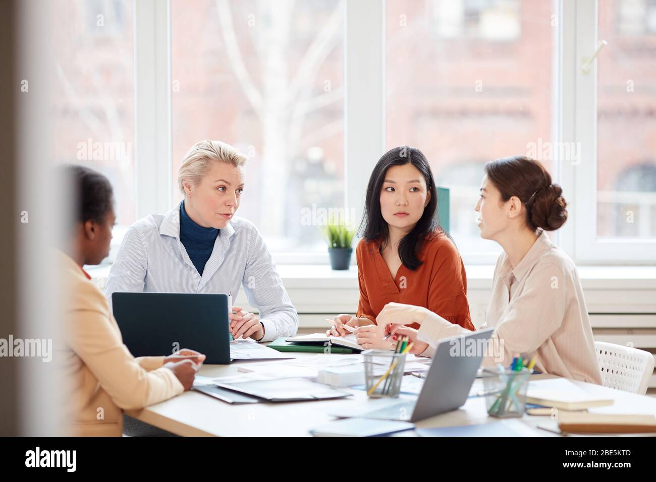 Portrait of diverse female business team discussing project while sitting at table during meeting in conference room against window, copy space Stock Photo