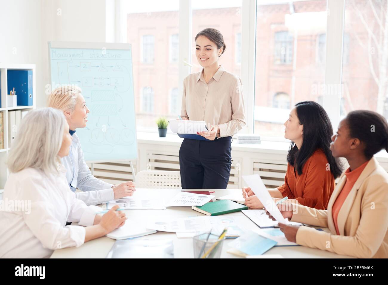 Portrait of smiling female manager presenting project plan to group of colleagues while standing by whiteboard during meeting in conference room, copy Stock Photo