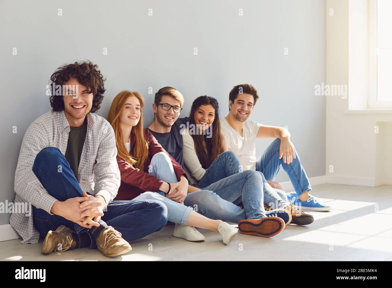 A group of friends is sitting on the floor in a room on a gray ...