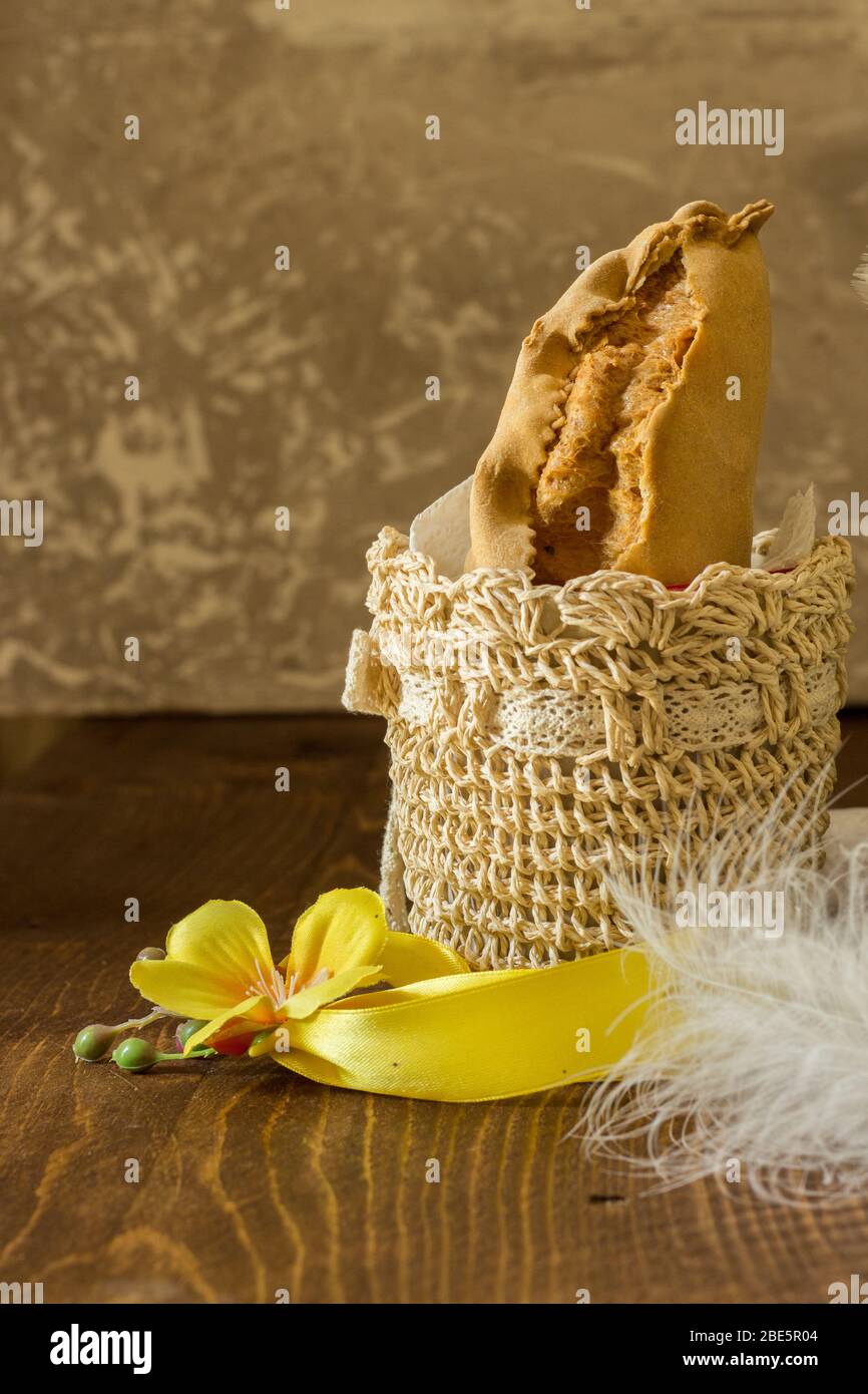 The image shows a typical Easter panzerotto from Campania inside a beige crochet basket with yellow and white feathers on dark wood and gray backgroun Stock Photo