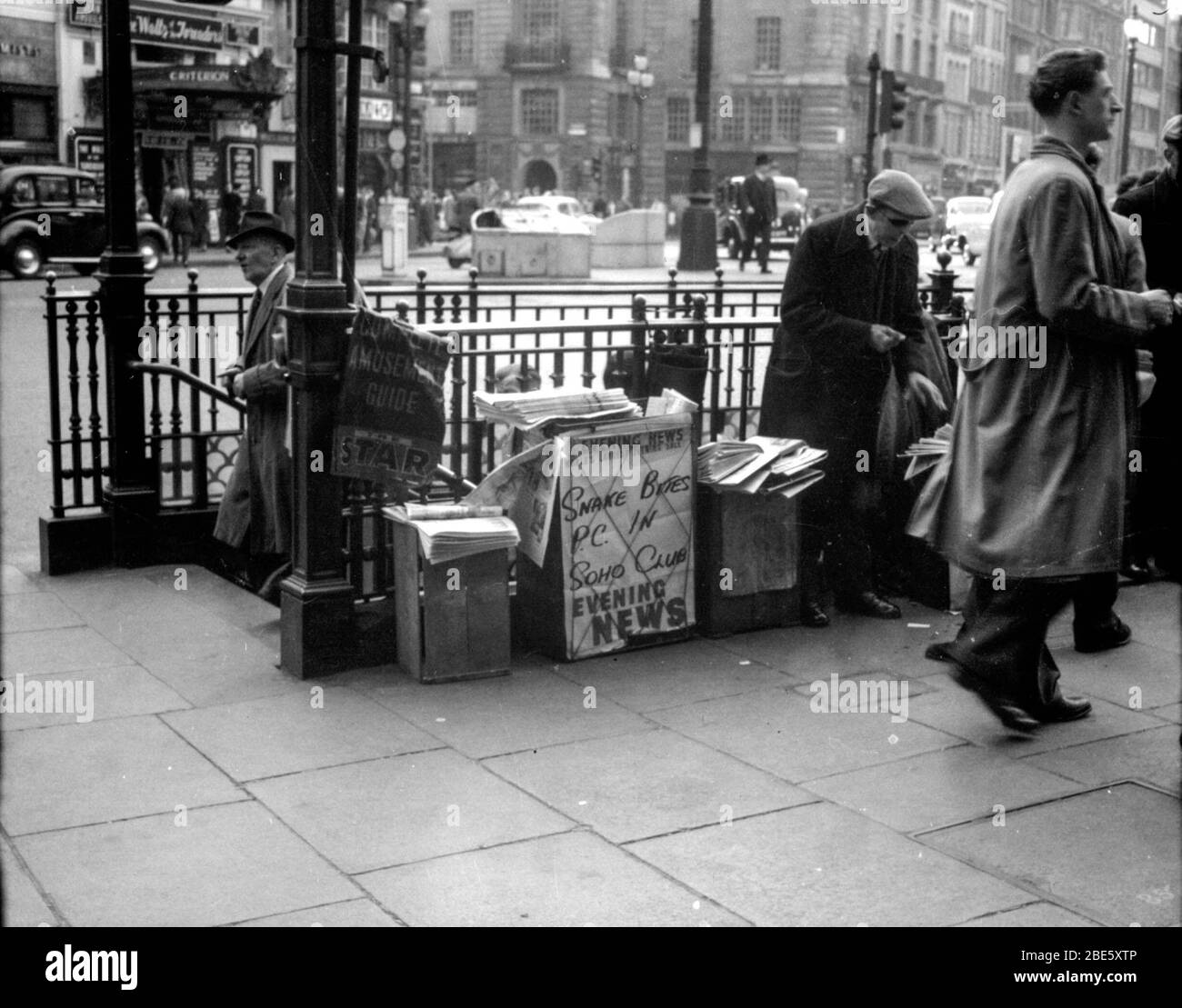 A man sells newspapers to London commuters at his newsstand in Piccadilly Circus, London in the 1930s. The headline in the Evening News is Snake Bites PC in Soho Club. Stock Photo
