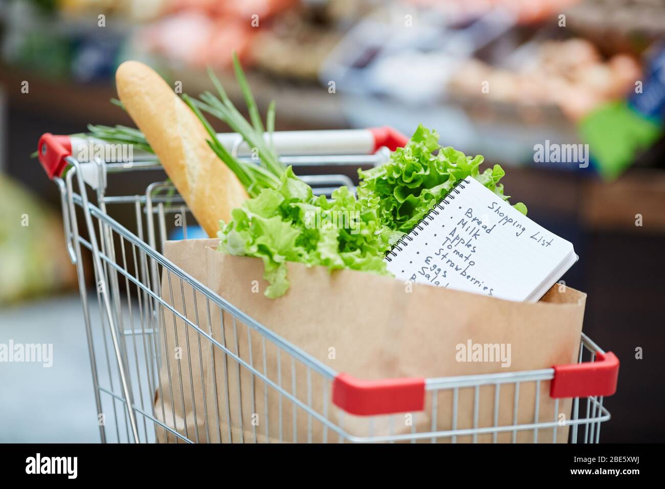 Background image of shopping cart with fresh groceries, focus on shopping list in paper bag, copy space Stock Photo