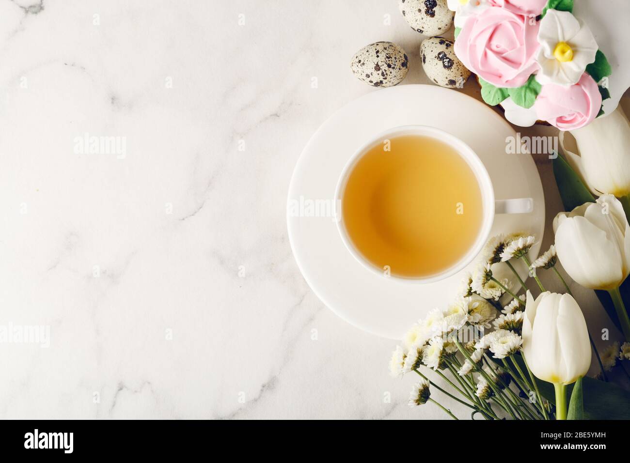 Easter breakfast. Homemade cake with cream roses on marble table. Cup of tea with flowers. Holiday concept. Top view, copy space Stock Photo
