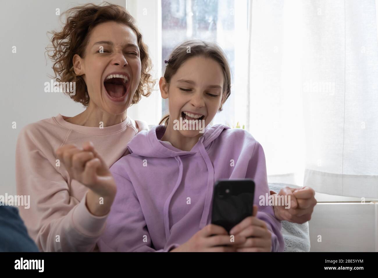 Excited mom and teenage girl daughter winning using smartphone Stock Photo