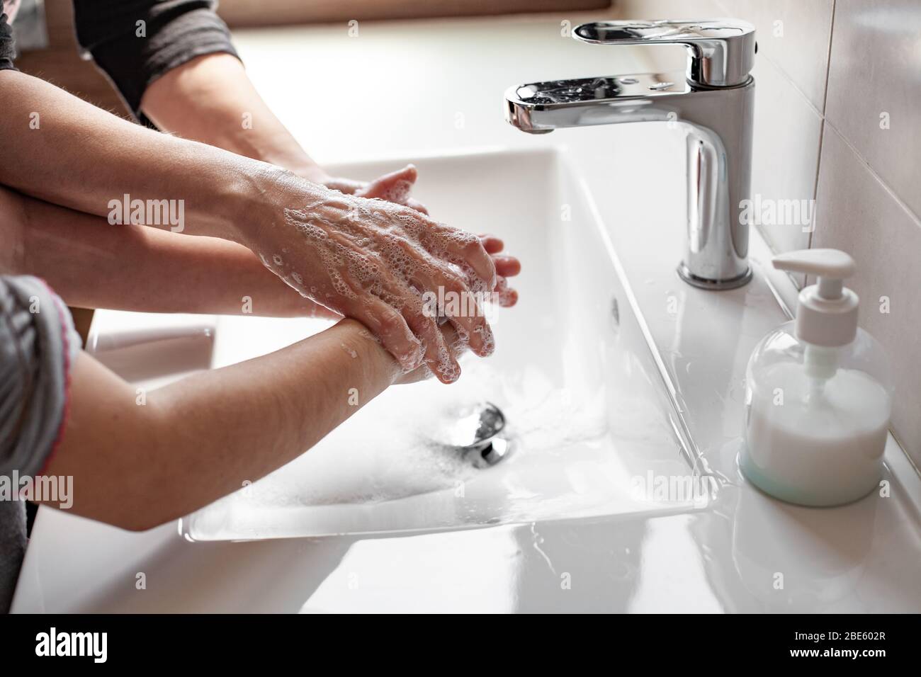Mother teaching her daughter how to properly wash their hands with soap to prevent coronavirus infection Stock Photo