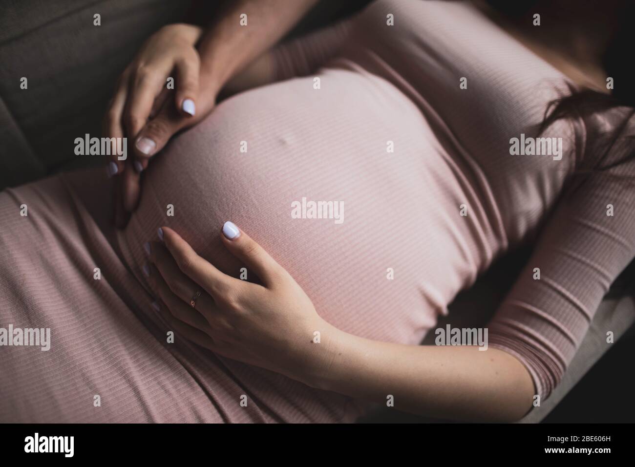 Male and female hands on a pregnant belly. The girl in the pink dress. Stock Photo