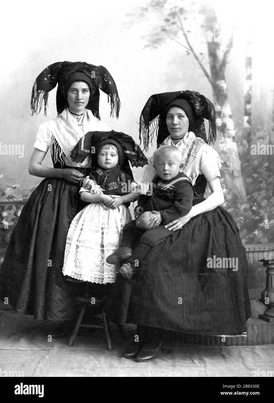 Spreewälderinnen.  These are traditional folklore costumes from the Spree (River) Forest, southeast of Berlin, Germany. This 1870s photo is from CottBus, Germany. Today's versions of these head-dresses are much more expanded and more colorful. Note the small shawl-like accessories on the women and the finely made dress on the little girl, who holds a doll. The boy, in a sailor uniform, holds a ball or mellon or ??  The women and girl each wear a cross on a necklace. The women wear simple but fine-looking shoes.   To see my other unusual vintage images, Search:  Prestor  vintage  odd  [or hats] Stock Photo