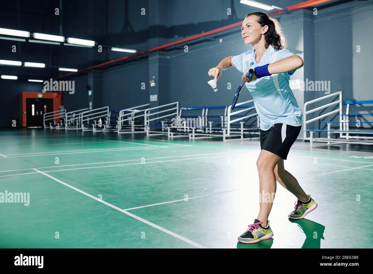 Pretty smiling young female badminton player serving shuttlecock when  playing in gymnasium Stock Photo - Alamy