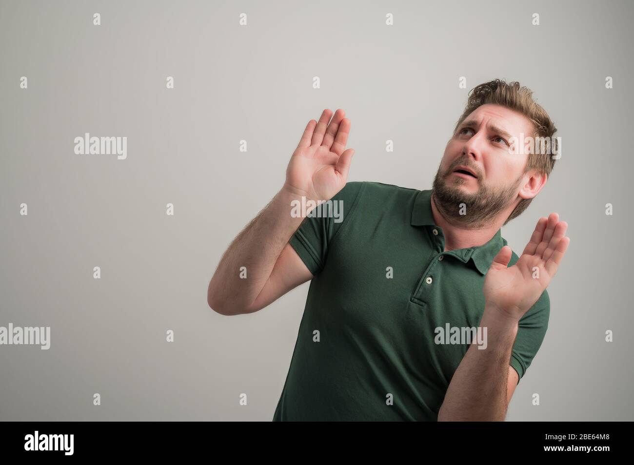 Portrait of serious stylish attractive man with thick beard, dressed in casual green t shirt making scary gesture isolated on gray background with cop Stock Photo