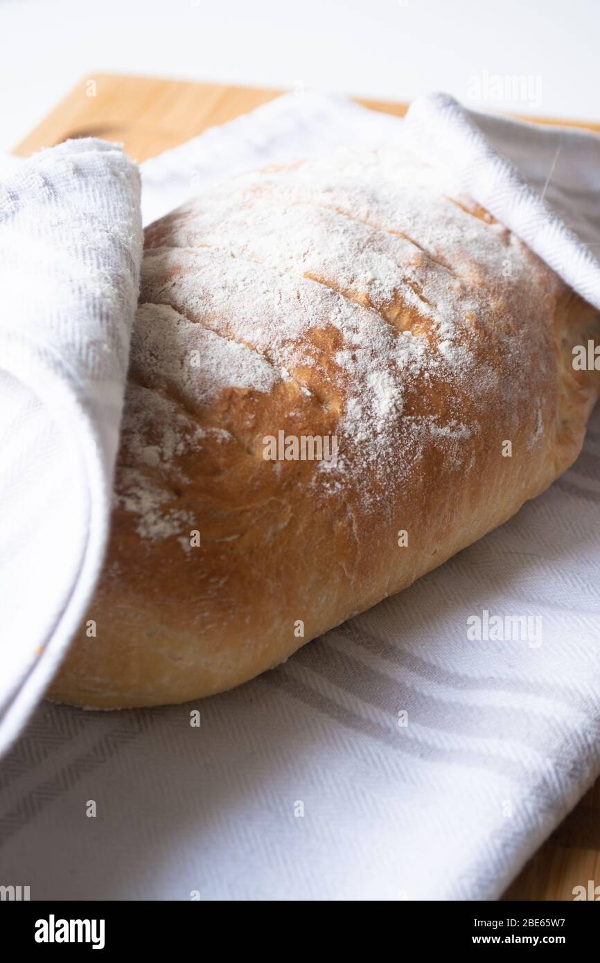 A loaf of homemade fresh bread with flour sprinkled on top in a kitchen ...