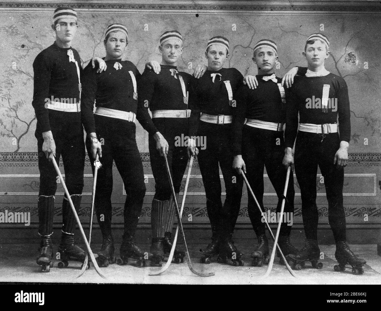 This is a Roller Polo team in the 1890s. Roller skating was big in 1870s USA, and when polo was brought in by James Gordon Bennett in 1876, the two sports quickly blended.  Roller polo was played with a ball. Roller rinks were converted to 40 by 80-foot courts with a chicken-wire goal cage at each end. The one-handed sticks were 1 inch in diameter and they played 3 15-minute periods. Players wore team uniforms and goalies wore more pads. Everybody wore Roller Skates.The man at right has a skate key hanging from his belt. To see my sports-related vintage images, Search:  Prestor  vintage  sport Stock Photo