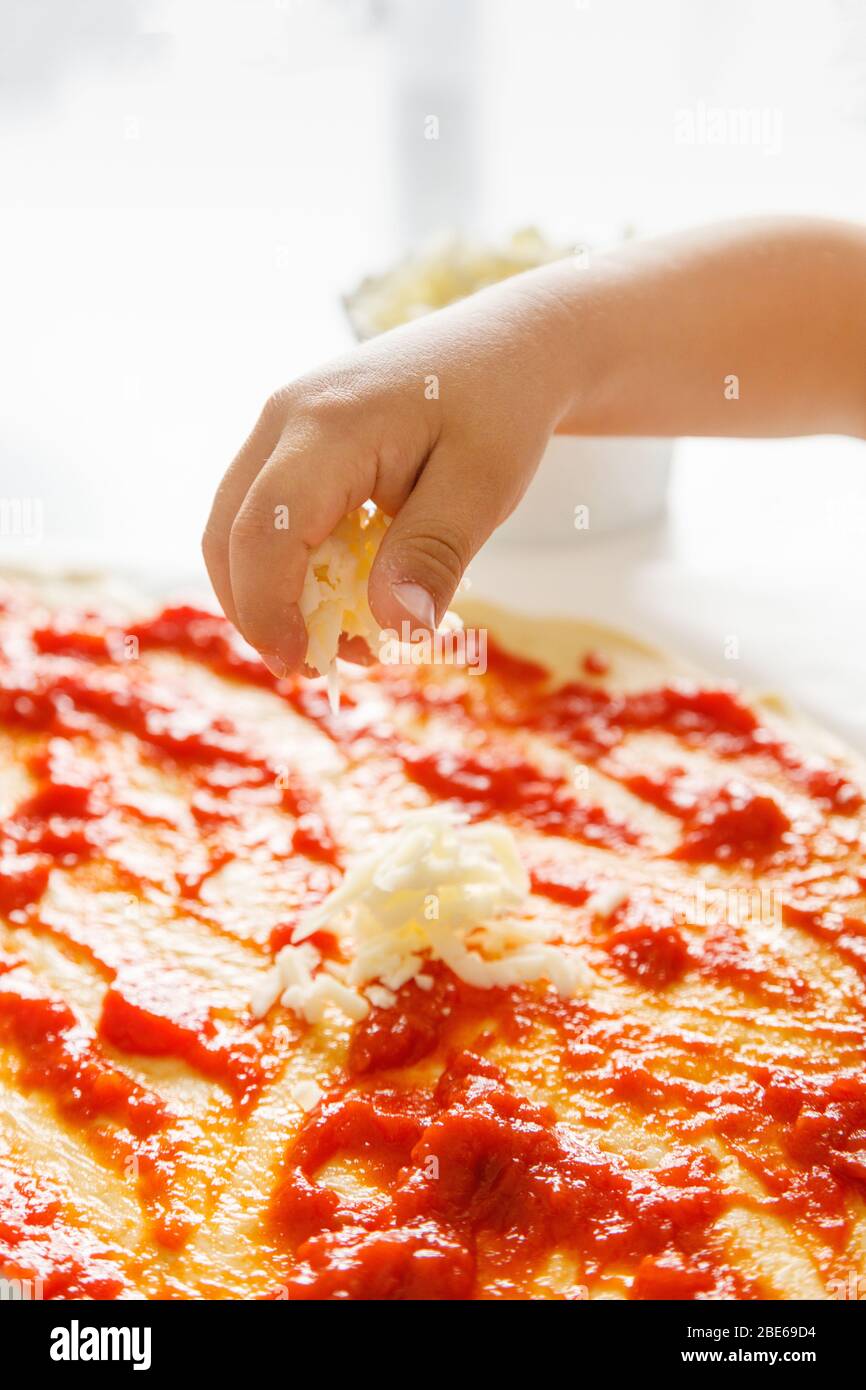 Hand of a small child throwing grated cheese on a pizza Stock Photo