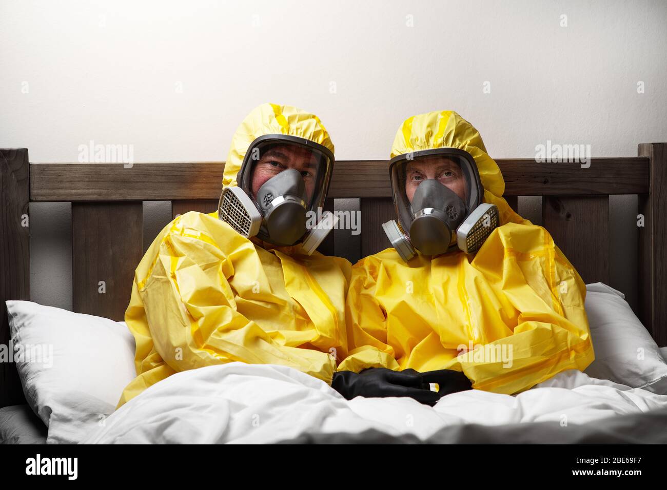 two people self isolating in bed being extra careful and wearing hazmat suit Stock Photo