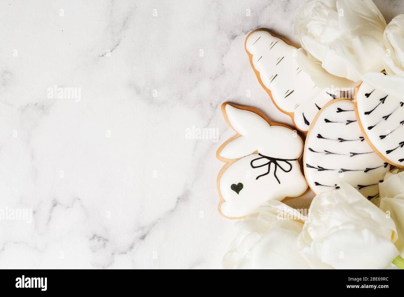 Easter gingerbread in shape of carrots and rabbits with bouquet of white tulips on marble table. Happy Easter concept. Minimalism background, top view Stock Photo