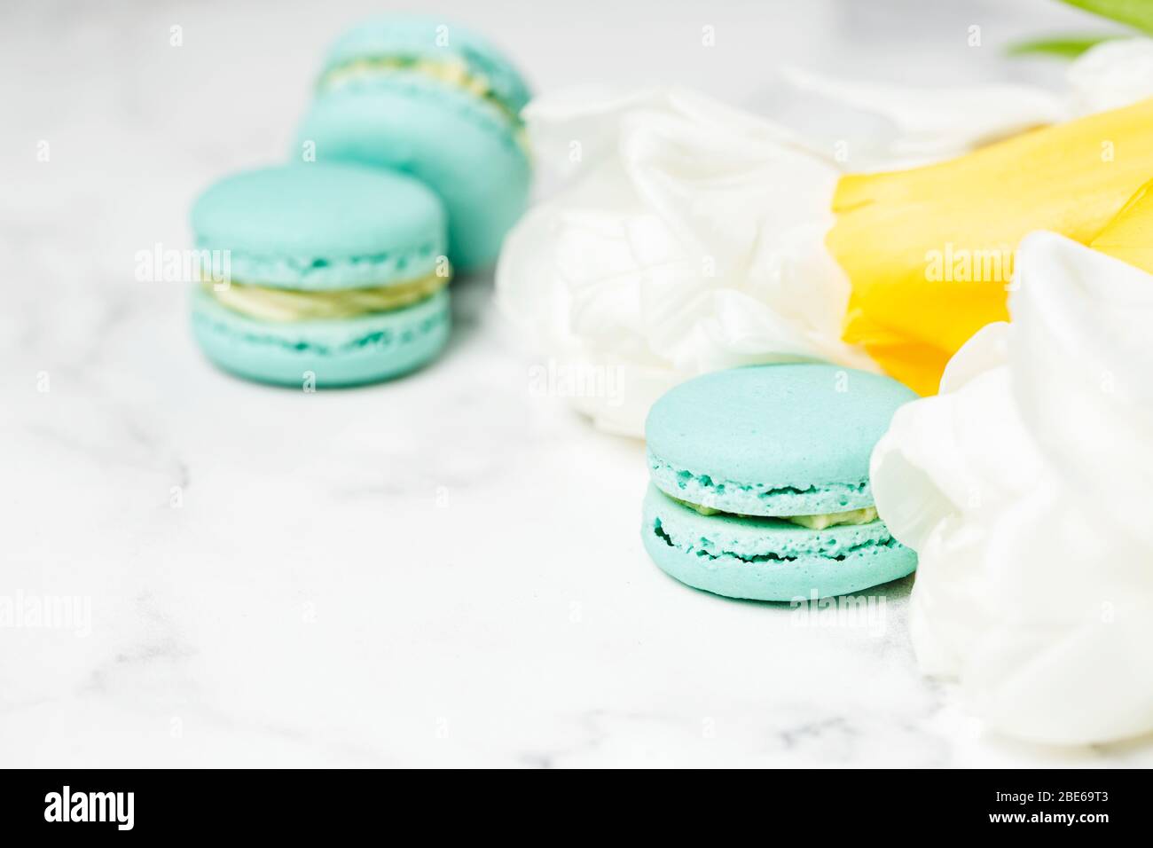 Macaroons closeup with white and yellow flowers on marble table. Mother's day concept Stock Photo