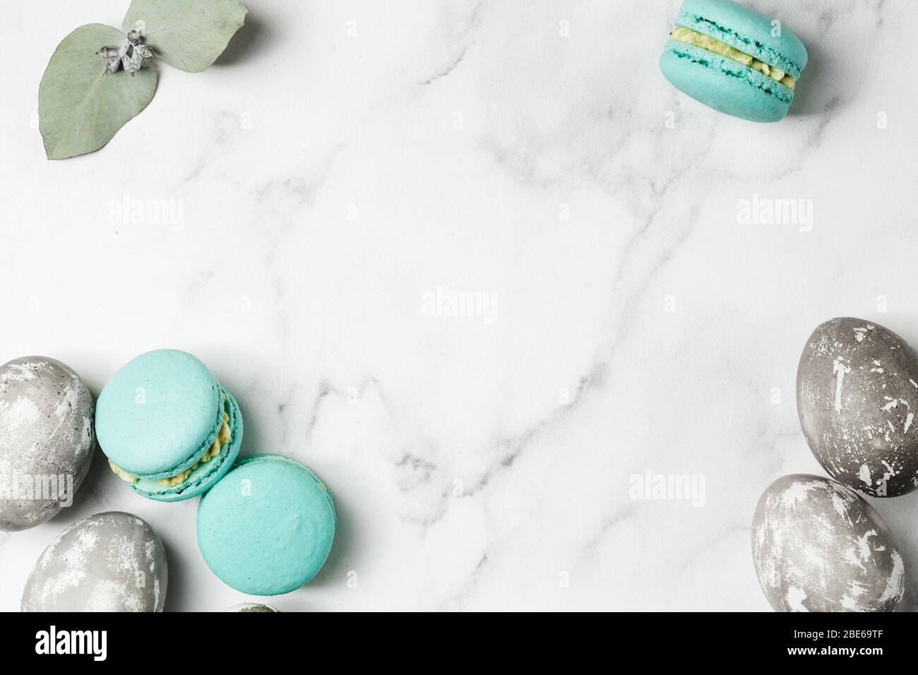Grey painted eggs, eucalyptus and turquoise macaroons on marble table. Happy Easter concept, copy space, top view Stock Photo