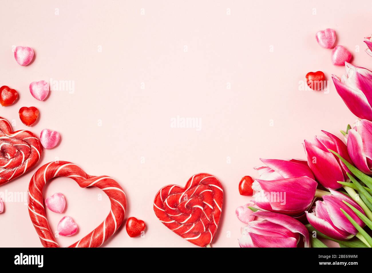 Heart shaped candies with peony tulips on pink background. Valentine's Day concept. Copy space Stock Photo