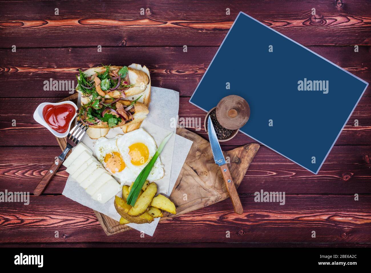 Big breakfast. Bruschettas, fried eggs, fried potatoes and cheese with sauce. There is a black pepper and cutlery and a place for text. Top view on a Stock Photo