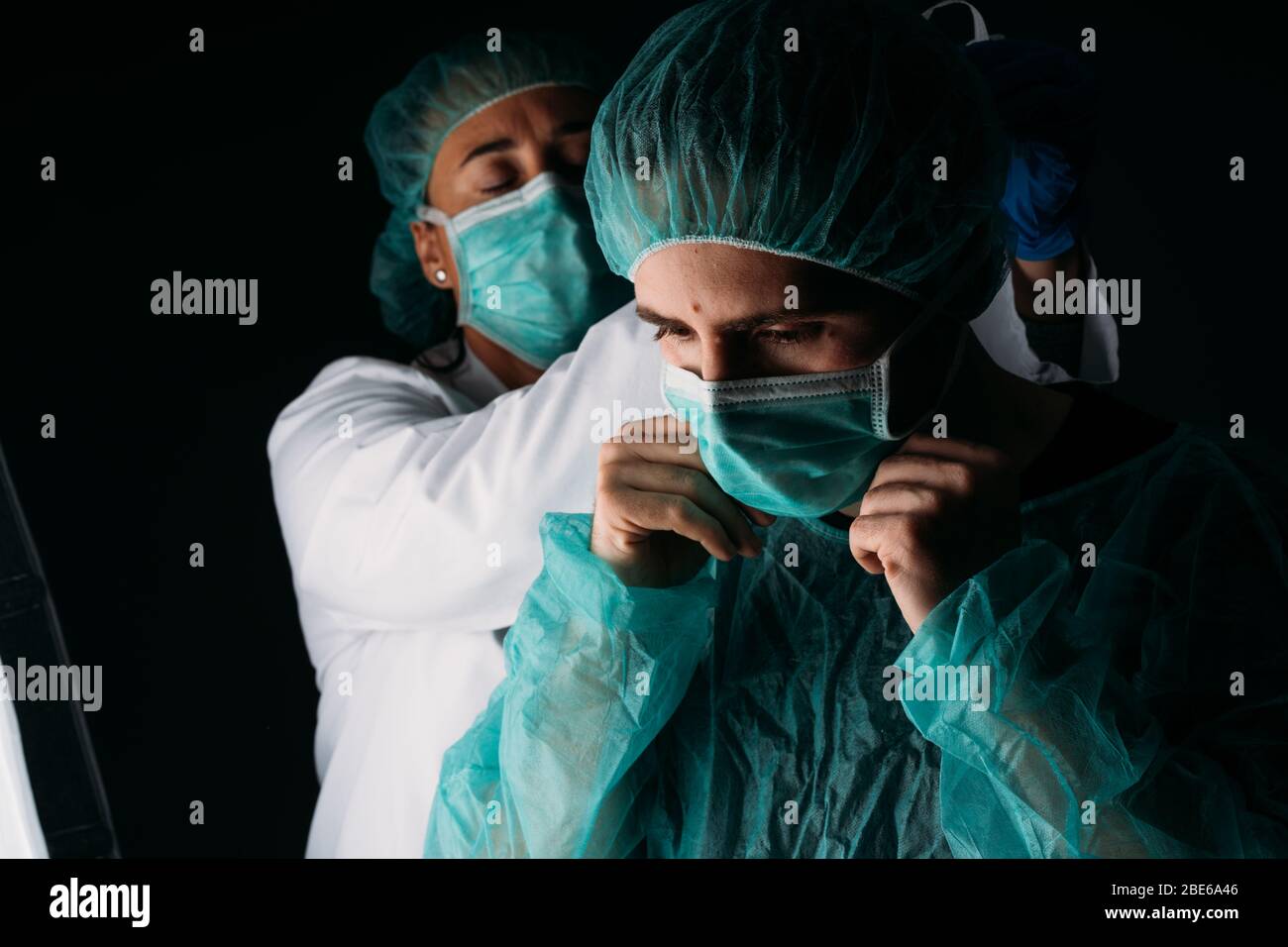 Portrait of two male and female doctors putting on mask to each other colleague working with medical surgical mask, medical cap and virus protective c Stock Photo