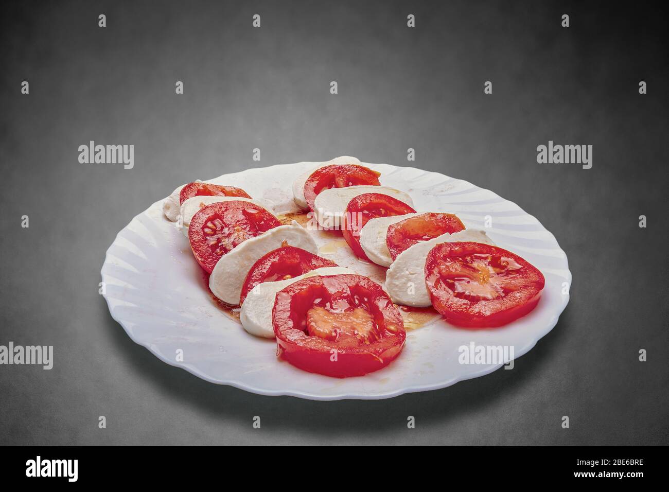 homemade red tomato salad with mozzarella and modena vinegar on white plate with gray textured background Stock Photo