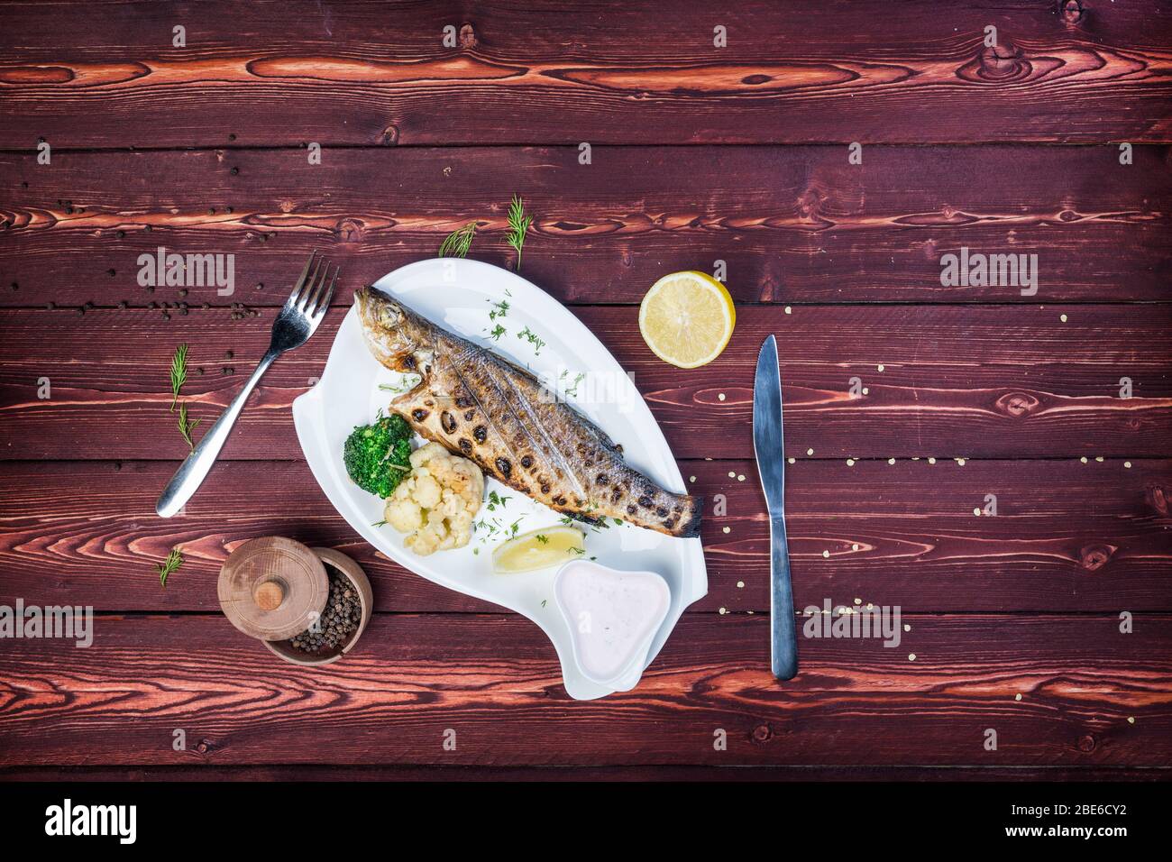 Grilled sea bass on a plate. Healthy food. Served Cauliflower and Broccoli. There is a black pepper and cutlery. Top view Stock Photo