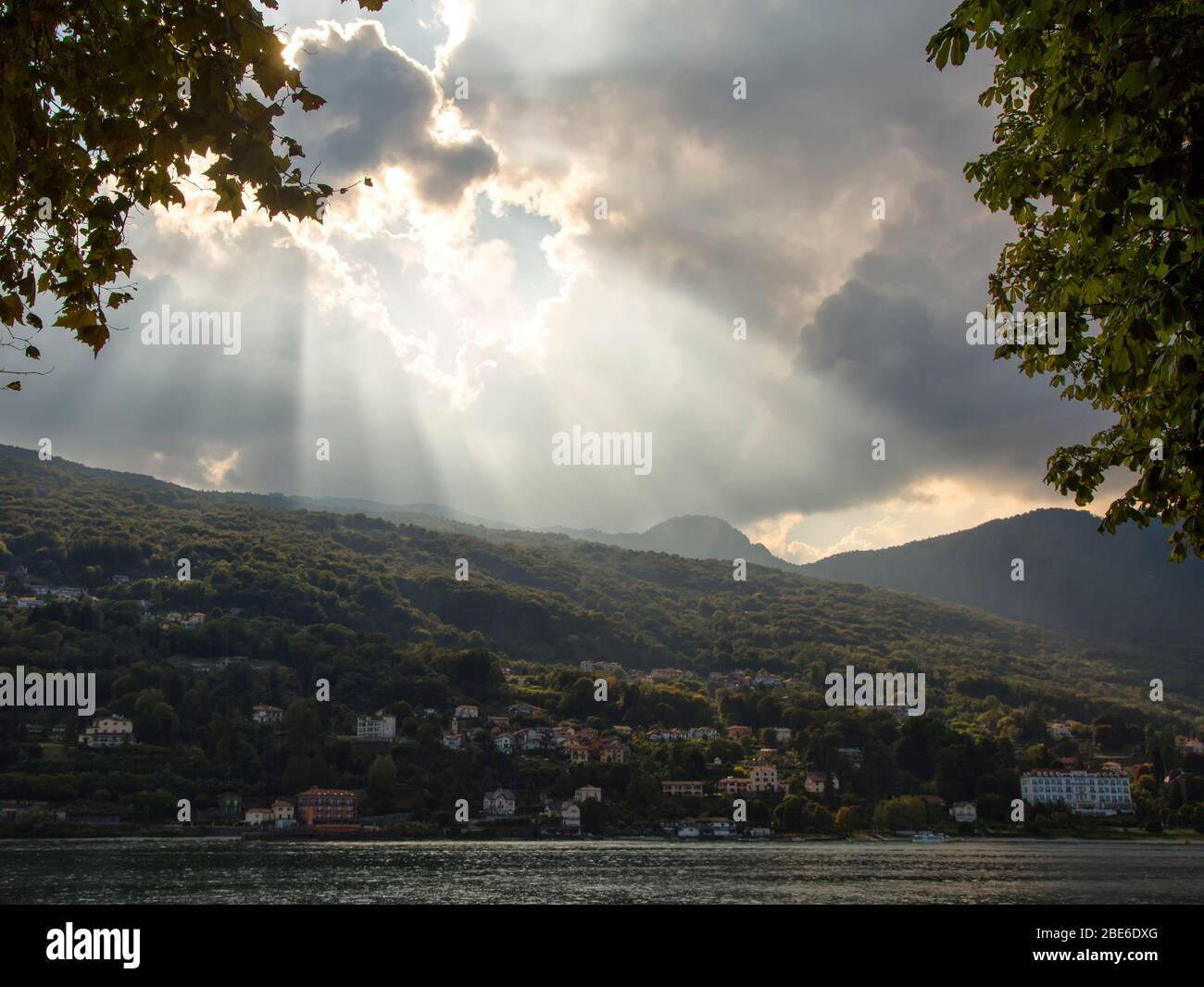 Sun coming out of clouds over mountains and lake Stock Photo