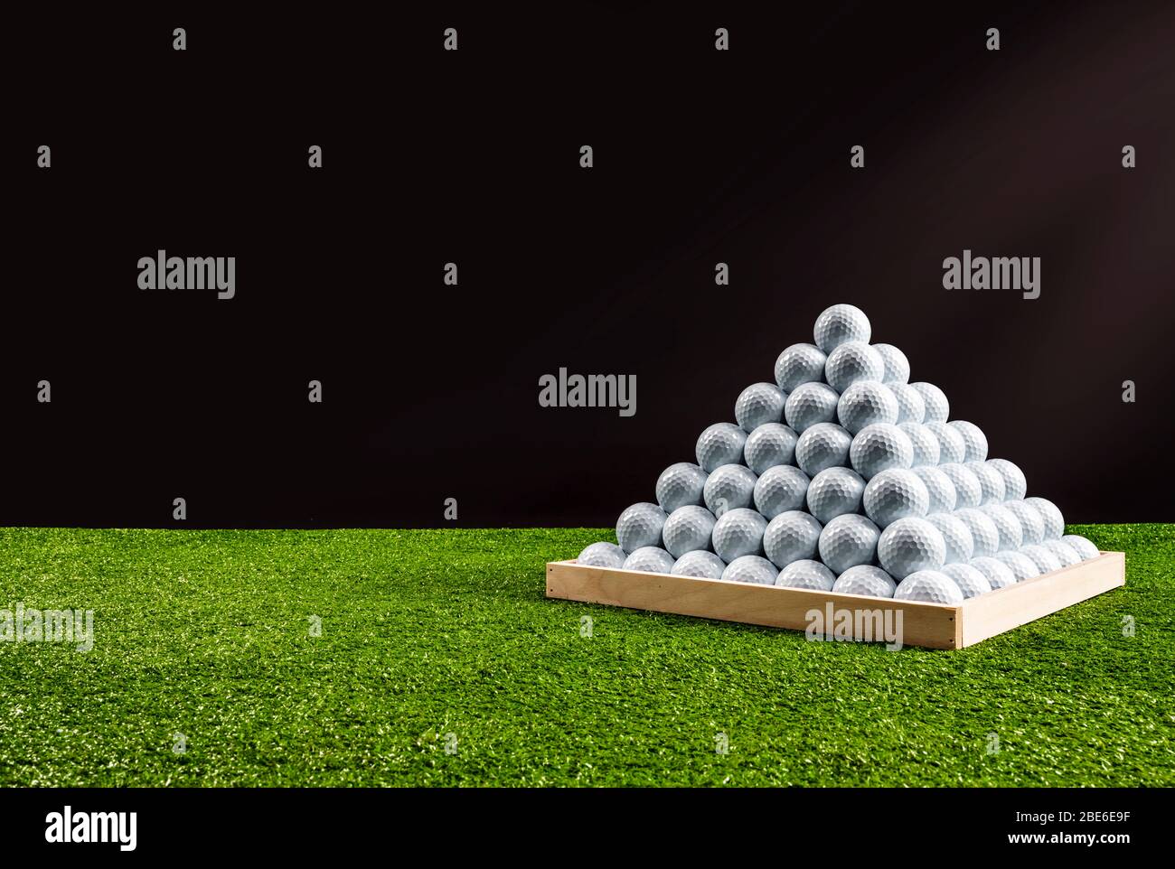 Pyramid of golf balls in a driving range, black background, horizontal