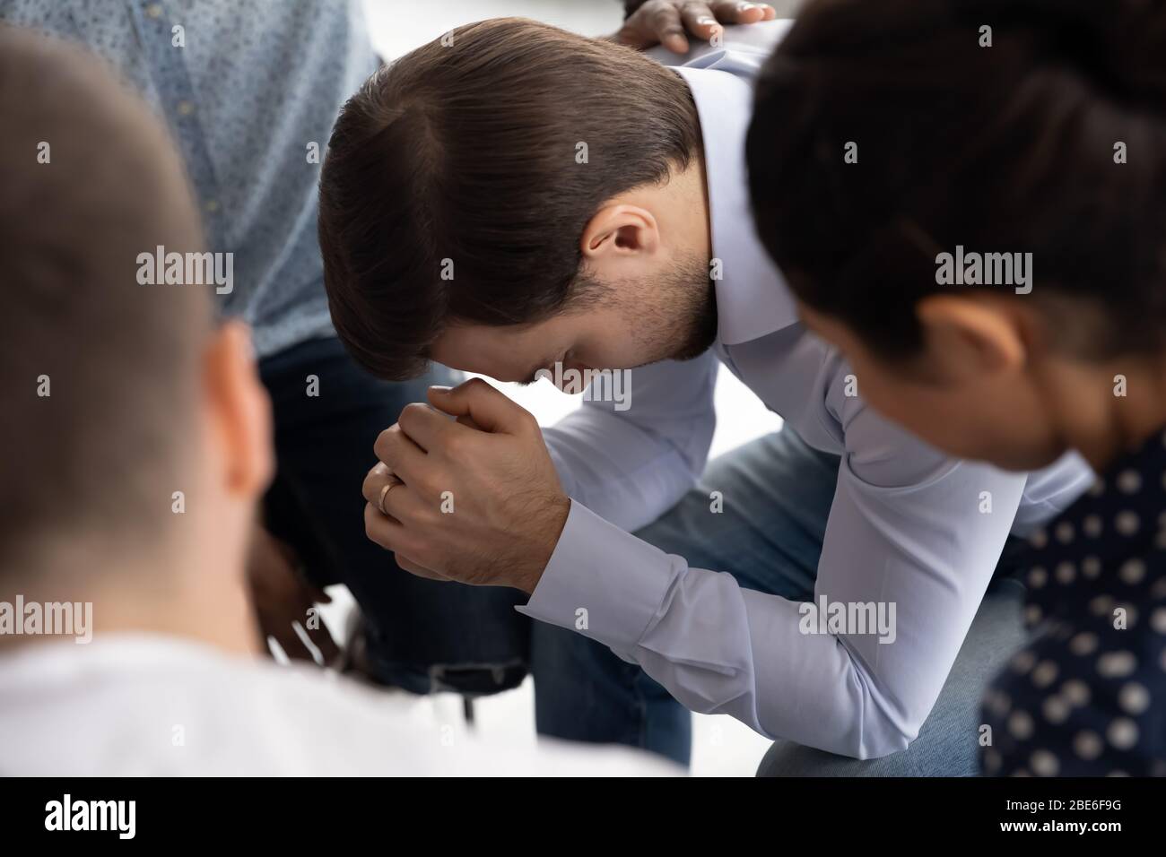 Diverse patients comfort depressed man at group therapy Stock Photo