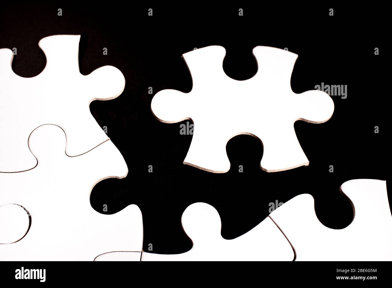 Unfinished white jigsaw puzzle pieces on black background Stock Photo