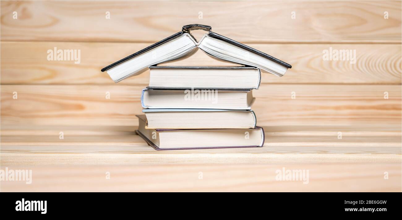 Quarantine background. Stay at home concept. House made with books piled on wooden background Read books background. COVID-19 impact. Basic rule of Stock Photo