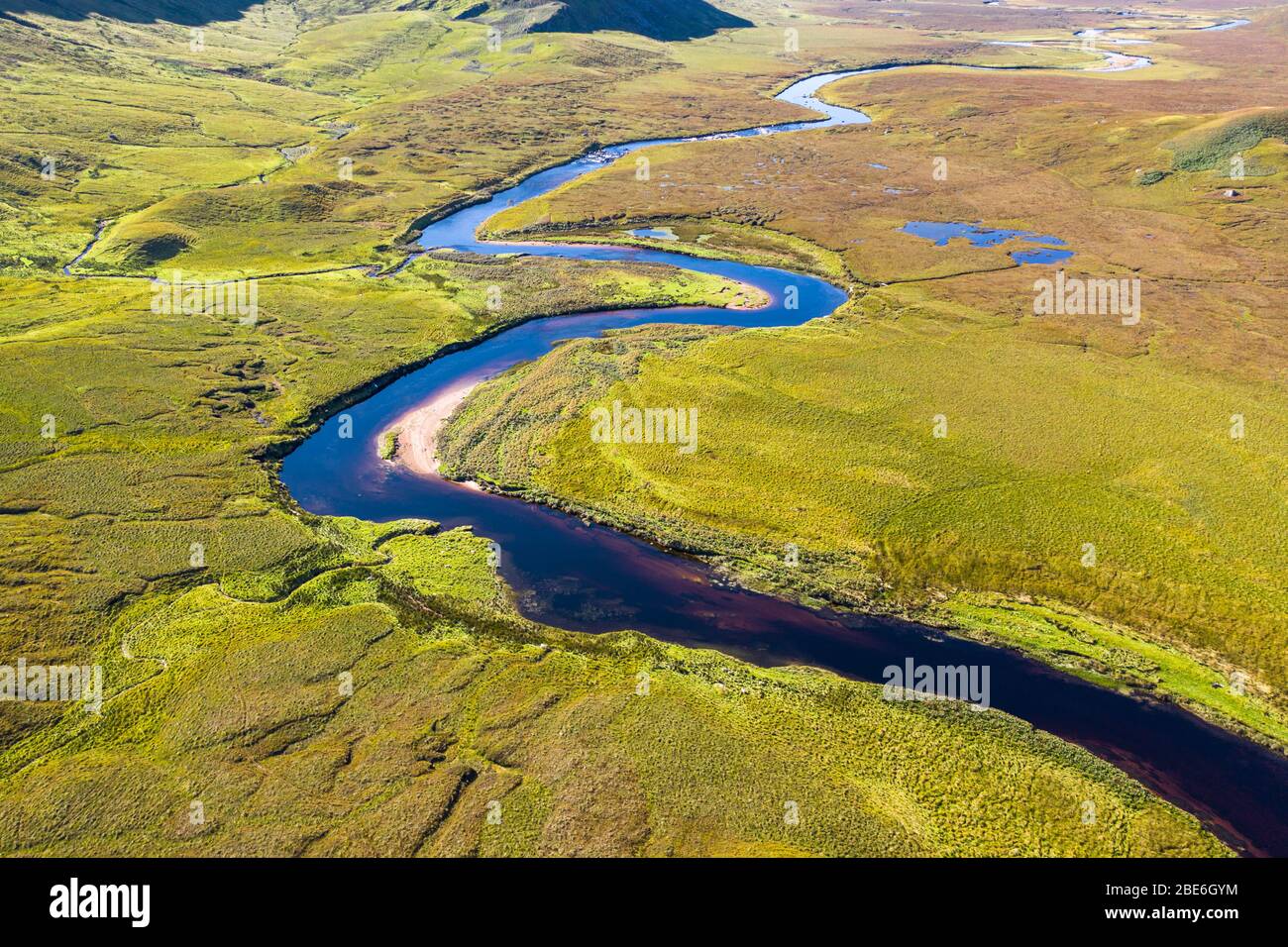 Drone shoot over s bend shape river across green valley by the Beinn Spionnaidh mountain at brigh autumnal day in the North West highlands of Scotland Stock Photo