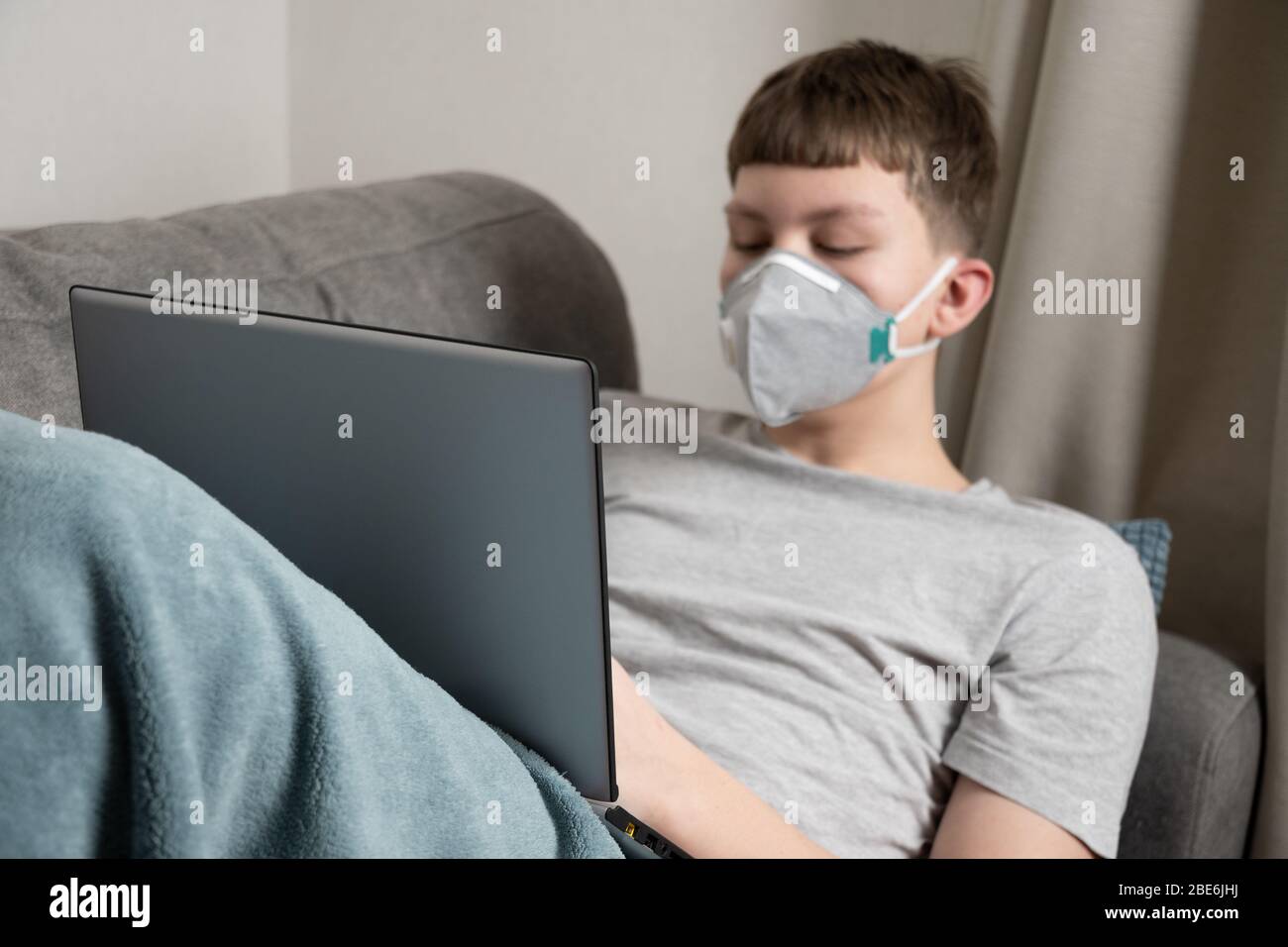 Teenager pass online education on laptop at home in medical mask against virus Covid 19. Prevention of Coronavirus. Close up. Stock Photo