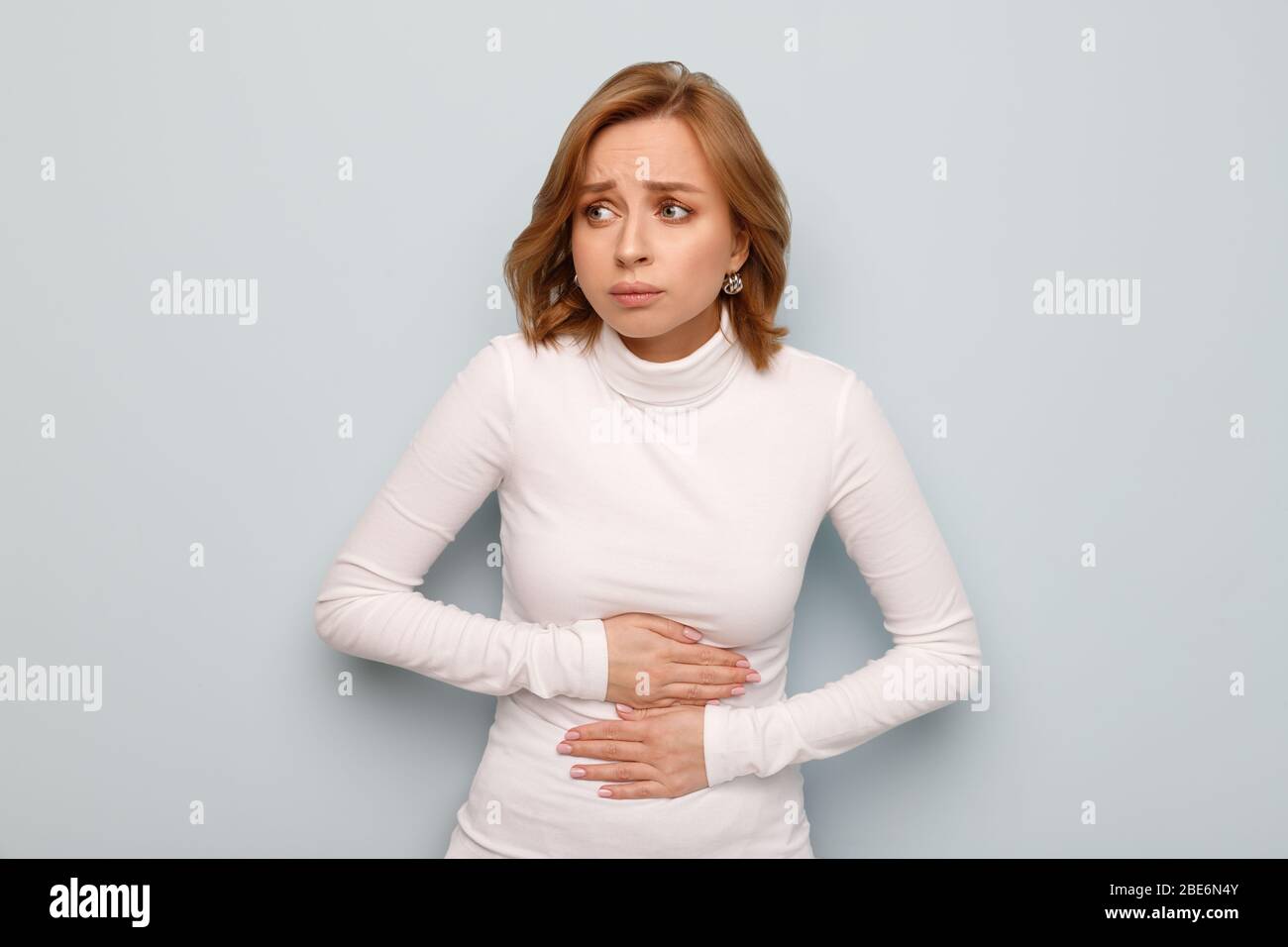 Health issues problems concept. Woman suffering from stomach pain, feeling abdominal pain or cramps, isolated on blue background.Period menstruation, Stock Photo