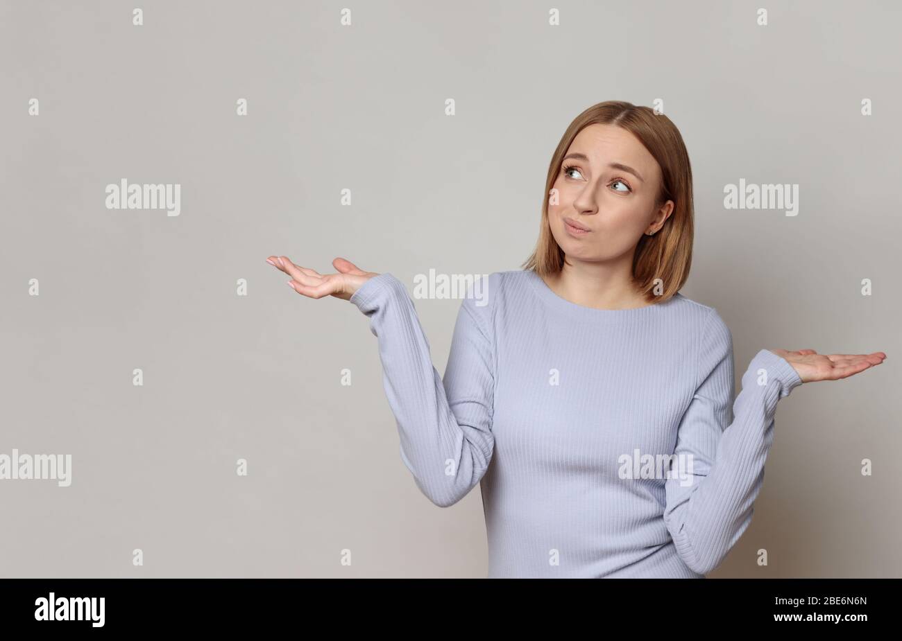 I don't know! Close up studio portrait of shy awkward young woman feeling embarrassed, confused and puzzled, shrugs shoulders, does not know what happ Stock Photo