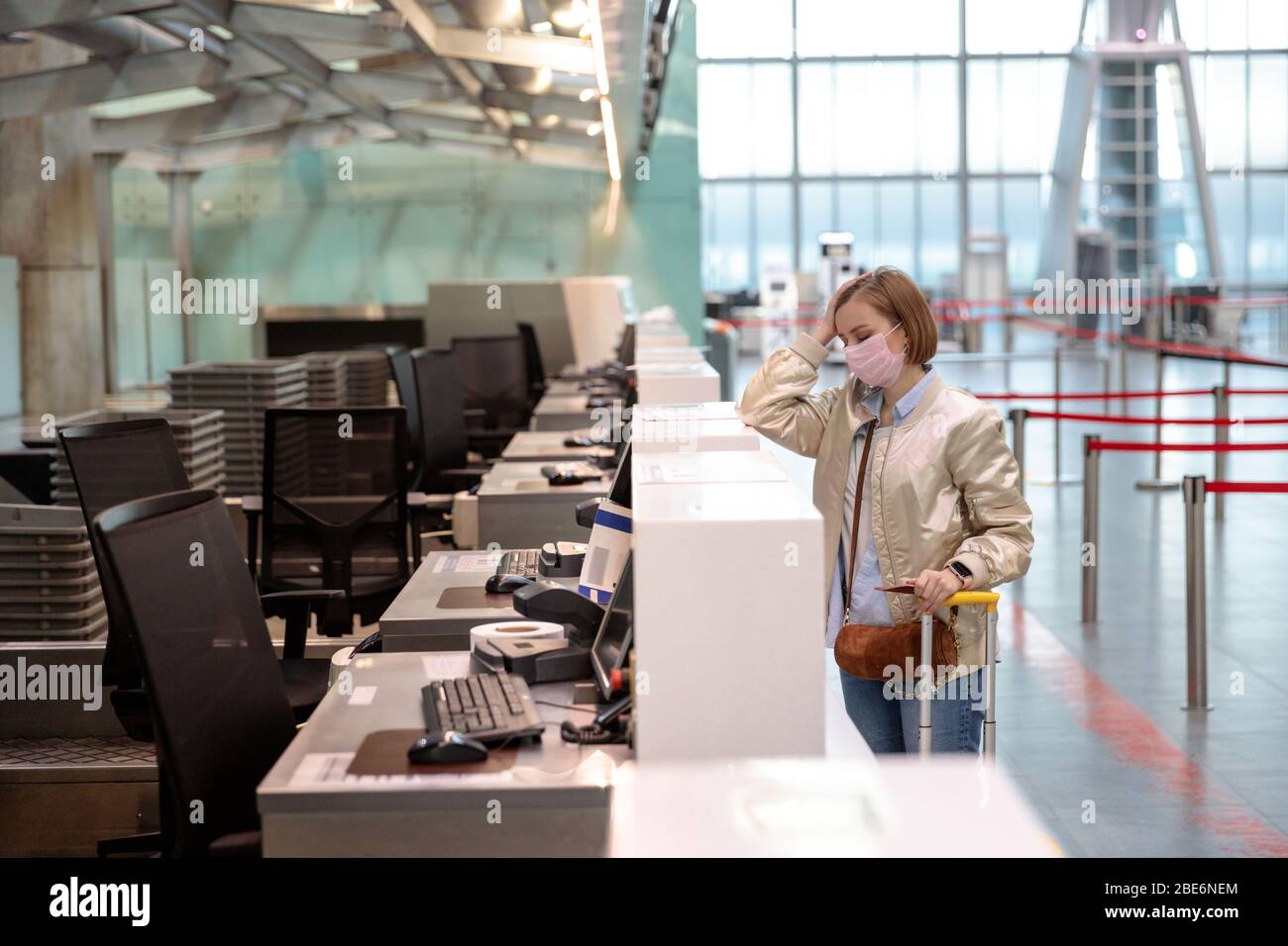 Woman with luggage over flight cancellation, stands at empty check-in counters at airport terminal due to coronavirus pandemic/Covid-19 outbreak trave Stock Photo