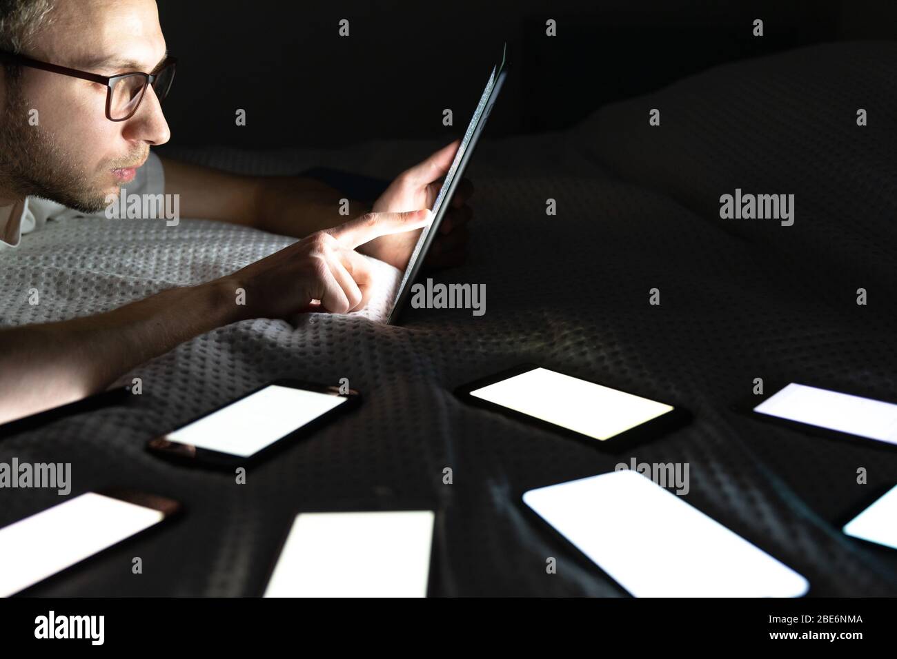 Addiction, nomophobia, insomnia, sleep disorder. Gadget addicted man using tablet at late night, chatting on social networks, lying in bed around the Stock Photo